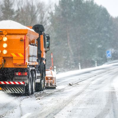 Snow plow on highway salting road. Orange truck deicing street at snowing time. Crystals dropping on asphalt. Maintenance winter vehicle in action.