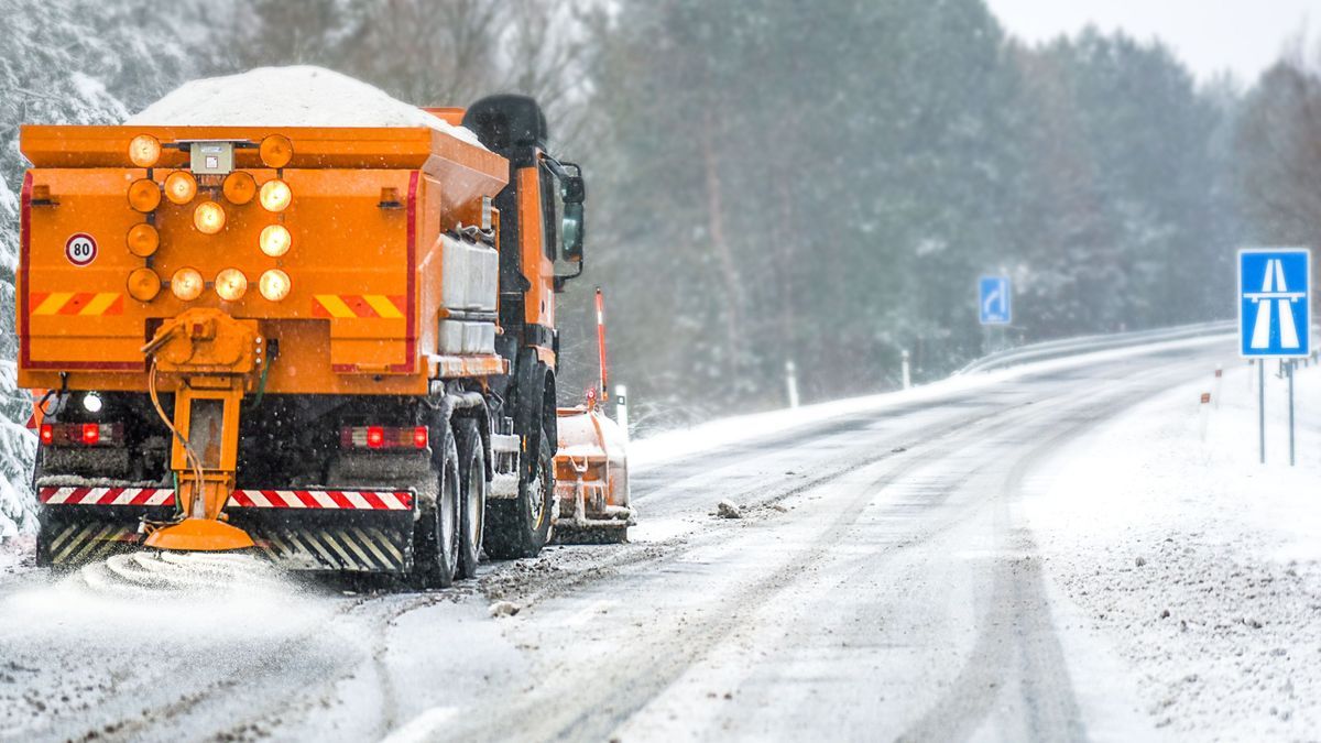 Snow plow on highway salting road. Orange truck deicing street at snowing time. Crystals dropping on asphalt. Maintenance winter vehicle in action.