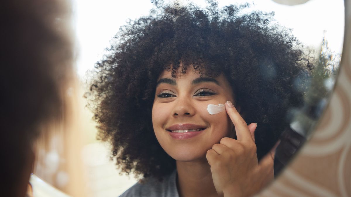 Beauty, cream and skincare with woman in mirror for product, facial and cosmetics. Morning routine, reflection and self care with face of female person and lotion at home for sunscreen and glow