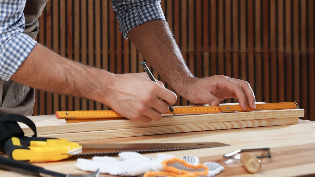 Handwerker / Heimwerker misst die Länge bei einem Holzbrett mit dem Zollstock und einem Bleistift