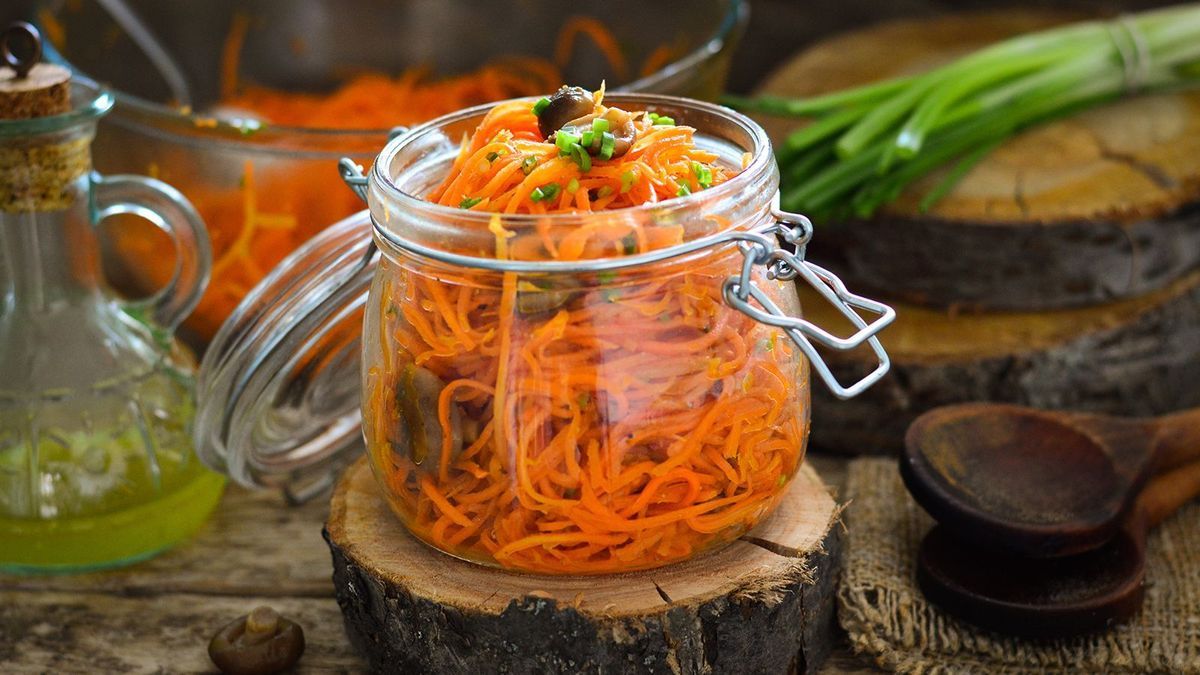 Carrot salad in a glass jar. Carrots in Korean with mushrooms. Wooden background.