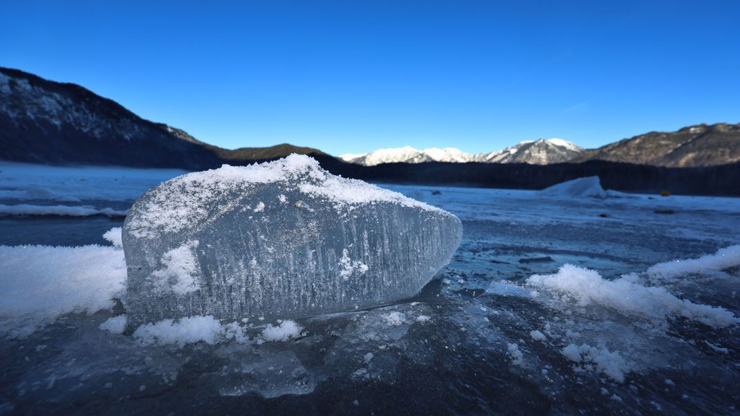 Ein Eisbrocken liegt auf dem mit einer Eisdecke überzogenen Eibsee.