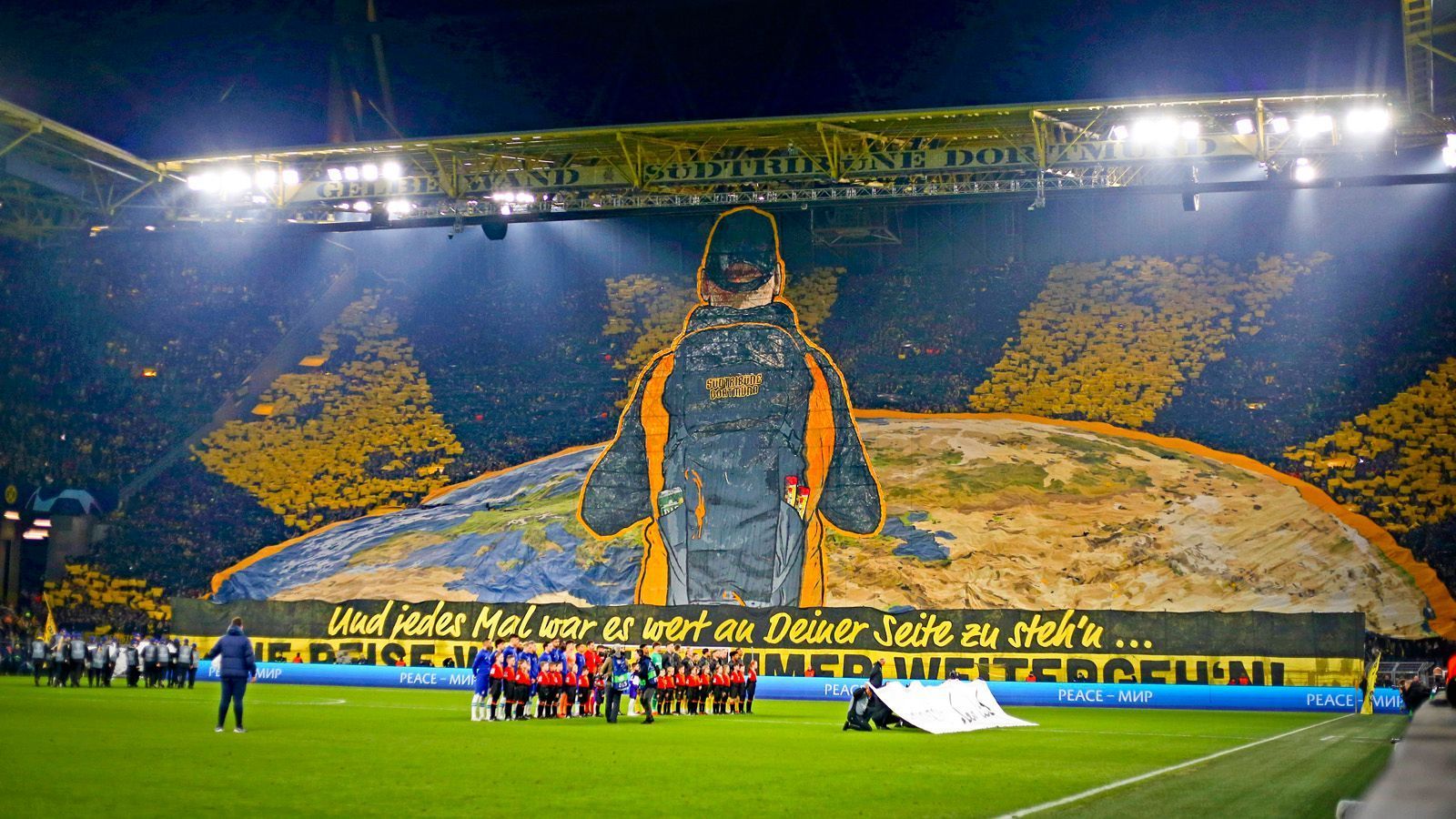 
                <strong>Borussia Dortmund - Fans gegen FC Chelsea mit XXL-Choreo</strong><br>
                Die Fans von Borussia Dortmund haben die beiden Duelle mit dem FC Chelsea mit einer die Südtribüne füllenden Choreografie eröffnet. Vor dem Hinspiel zogen die Anhänger ein XXL-Banner hoch. "Und jedes Mal war es wert an Deiner Seite zu steh'n" stand unter dem Kunstwerk. Eine Hommage an den BVB, aber auch an die Fans, die ihre Mannschaft immer und überall unterstützen. Ob nun in Dortmund oder auf der ganzen Welt.
              