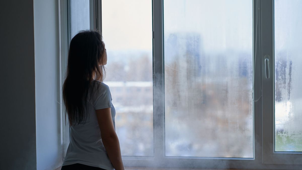 Cold winter weather. Woman step to window, open it and frosty air rushes from outside through open windows to apartment. Airing housing in cold winter