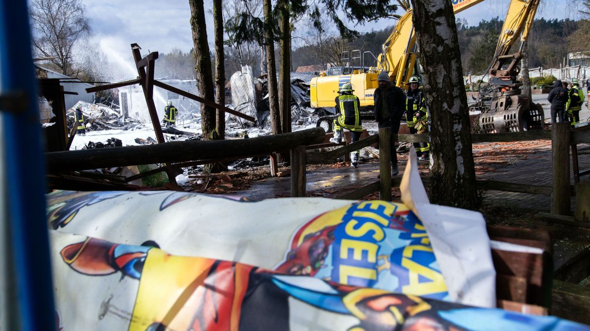 Ein Banner, auf dem Teile des Schriftzugs «Freizeit-Land Geiselwind» zu erkennen sind, hängt über einem Geländer, während Einsatzkräfte der Feuerwehr im Hintergrund mit Löschschaum sprühen.