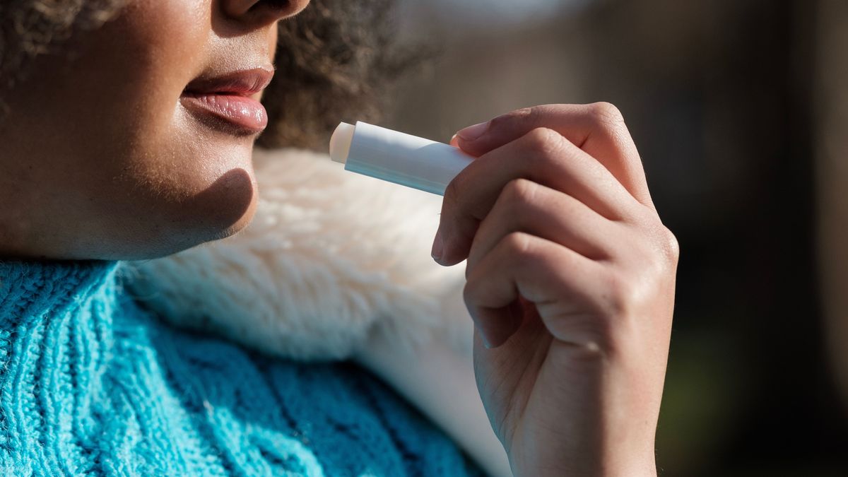 Unrecognizable curly woman applying lip balm to protect lips.