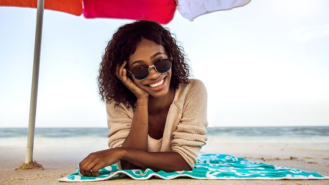 Platziert euch unter einen stylischen Sonnenschirm am Strand und seid so den schädlichen UV-Strahlen nicht direkt ausgesetzt.