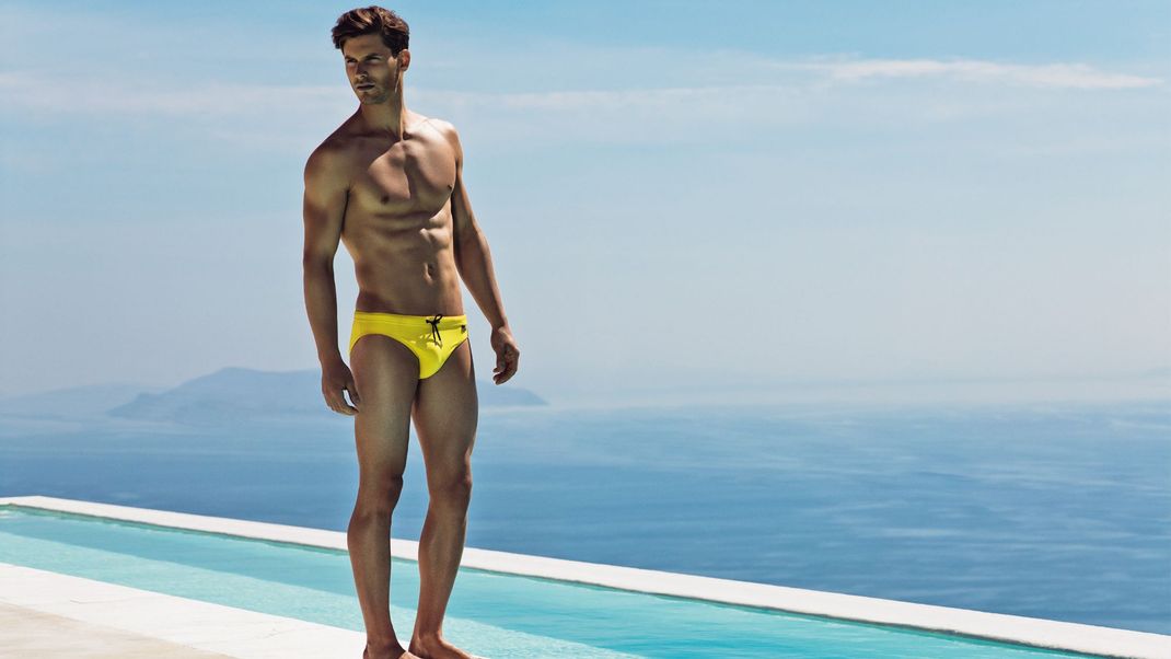 Ein männliches Modell trägt eine klassische Badehose in Slip-Form.