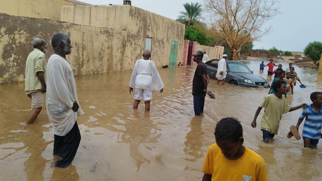 Menschen waten durch eine vom Hochwasser überschwemmte Straße im Sudan.