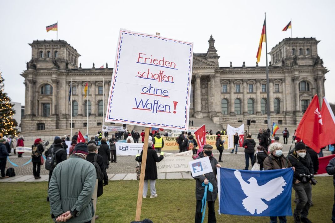 Menschen stehen beim bundesweiten Aktionstag "Abrüsten statt Aufrüsten" im Dezember 2020 vor dem Bundestag. Den Spruch "Frieden schaffen ohne Waffen!" verwendete bereits eine Bewegung in den 1980er-Jahren in der DDR.