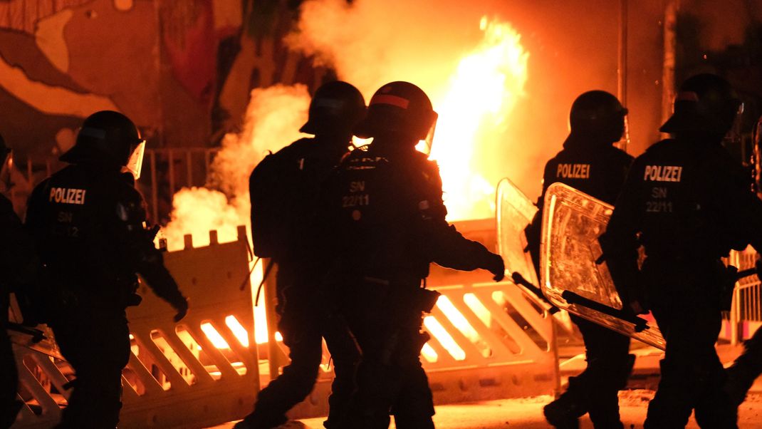 Polizisten gehen an einer brennenden Barrikade vorbei. 