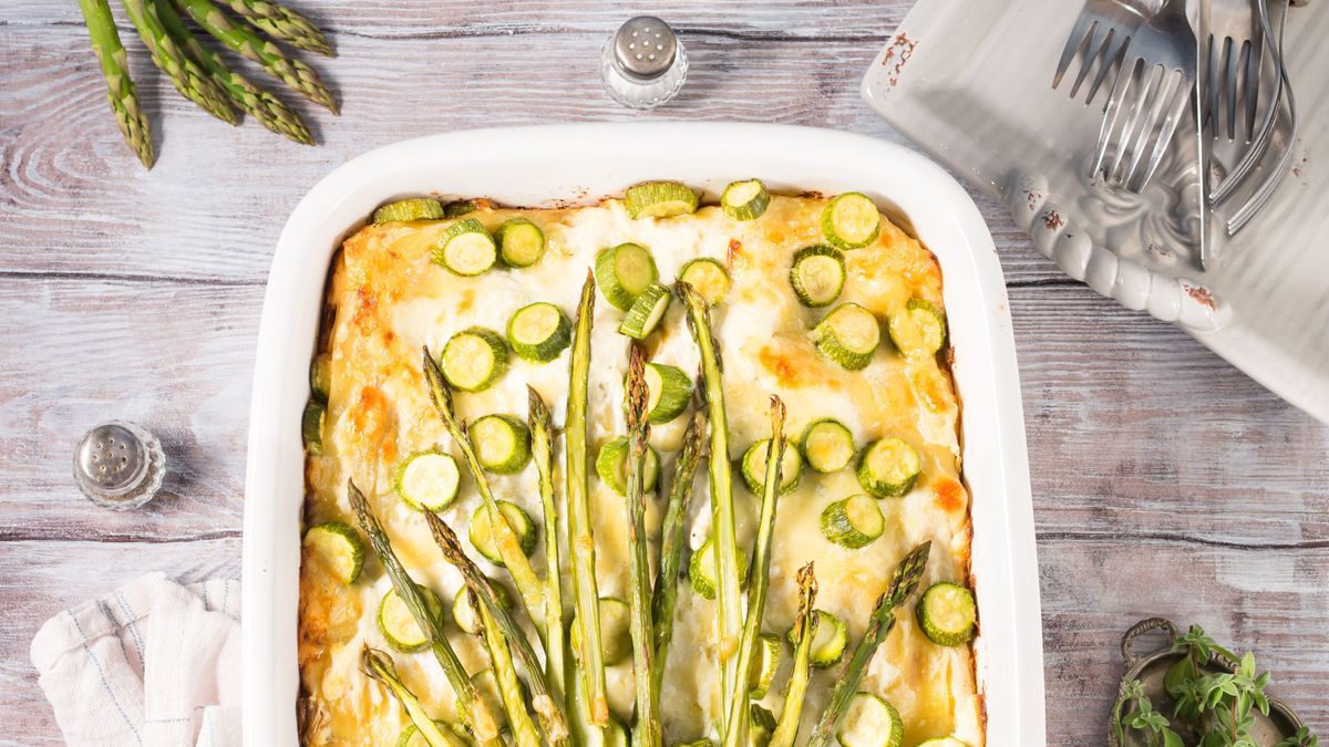 Home made asparagus lasagna casserole with zucchini, ricotta, mozzarella cheese and marjoram herb in a ceramic tin on wooden table. Rustic spring baked one plate food
