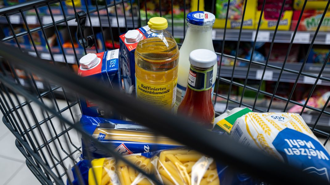 Lebensmittel wie Milch und Pasta liegen in einem Einkaufswagen in einem Supermarkt.