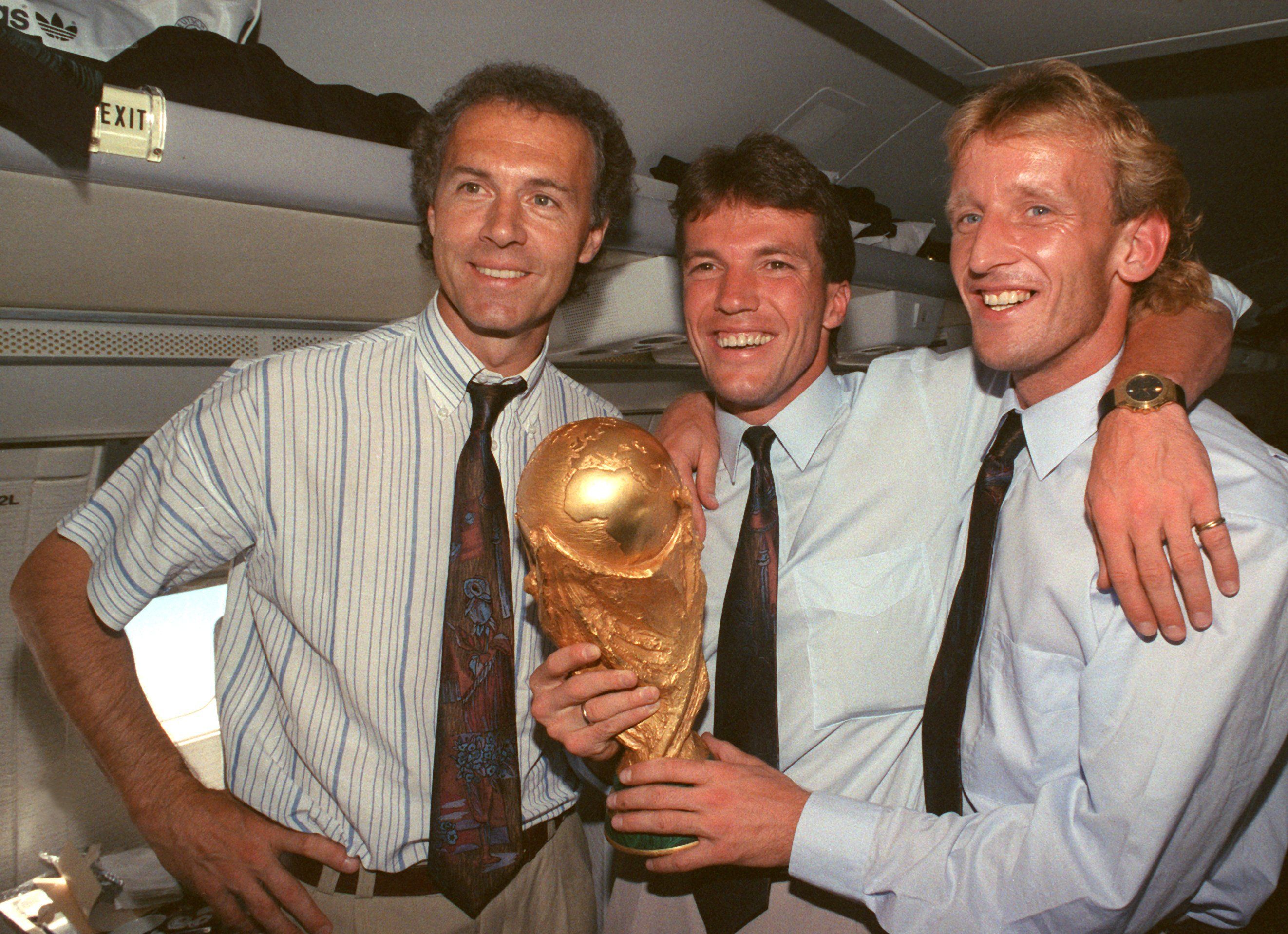 Juli 1990: Im Flugzeug beim Rückflug von Rom nach Frankfurt präsentieren der damalige DFB-Teamchef Franz Beckenbauer (links), Kapitän und Mittelfeldspieler Lothar Matthäus (Mitte) und Abwehrspieler Andreas Brehme, der das entscheidende Tor schoss, den gewonnenen WM-Pokal. 