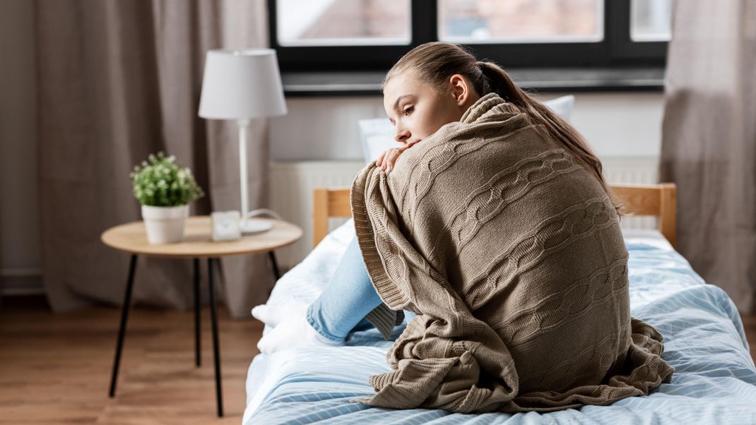 sadness and people concept - sad girl in blanket sitting on bed at home || Modellfreigabe vorhanden