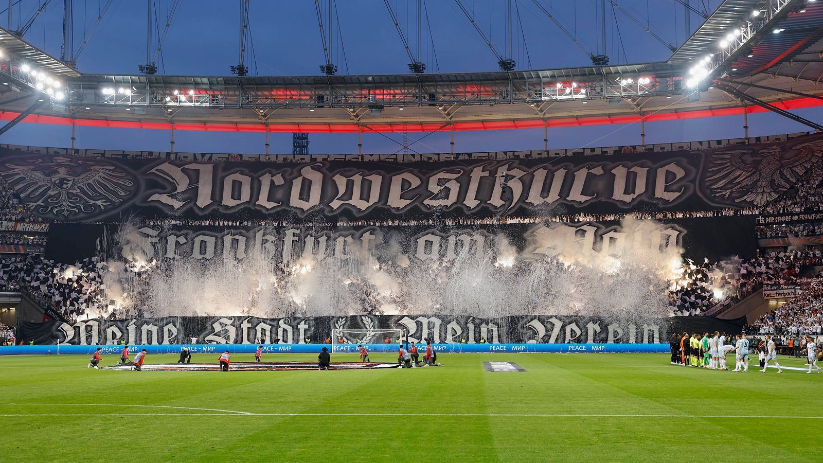 
                <strong>Heimspiel gegen West Ham United (5. Mai 2022)</strong><br>
                Im Halbfinal-Rückspiel gegen West Ham United sorgten die Eintracht-Anhänger schon zuvor für eine beeindruckende Choreographie. Dabei wollten die Frankfurt-Fans vor allem ihre Liebe zur Stadt und dem Verein ausdrücken. "Nordwestkurve Frankfurt am Main" und "Meine Stadt, mein Verein" war auf riesigen Bannern zu lesen, die von einer Pyro-Leuchtshow begleitet wurden. Außerdem schmückten die Adler des Vereins- bzw. Stadtwappens die oberen Ränder der Choreographie. Ein würdiger Auftritt der Eintracht-Fans an diesem einzigartigen Abend.
              