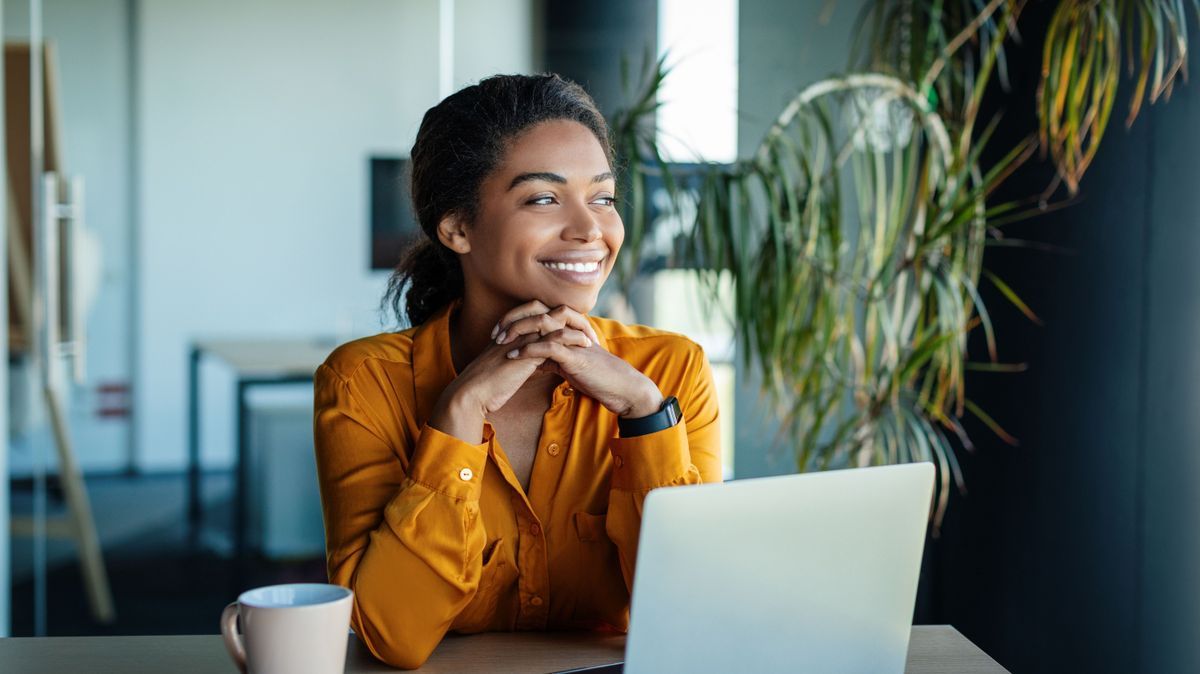 Portrait of dreamy african american businesswoman sitting at desk in office and thinking while working on laptop