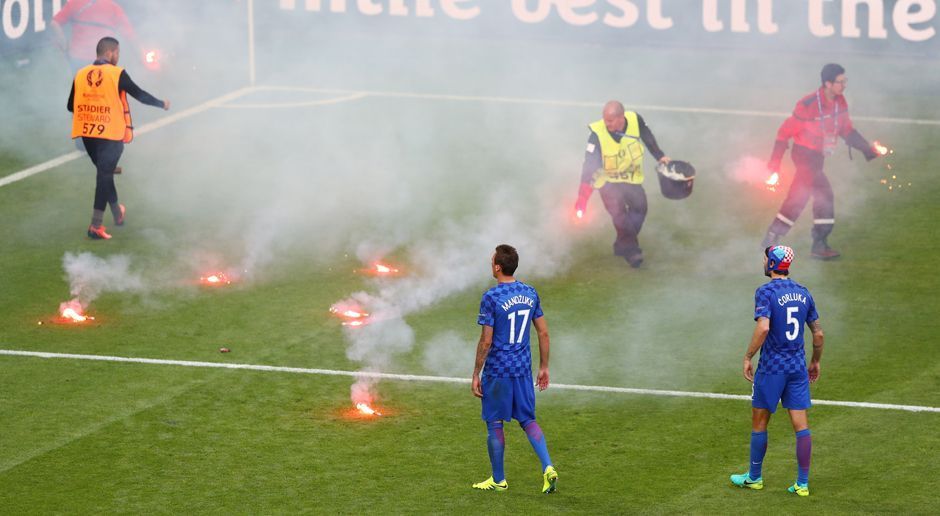 
                <strong>Die Schande von St. Etienne</strong><br>
                Sofort eilen Ordner herbei, um die gefährlichen Fackeln vom Rasen zu sammeln. Die kroatischen Spieler versuchen, den aufgebrachten Fanblock zu beruhigen.
              