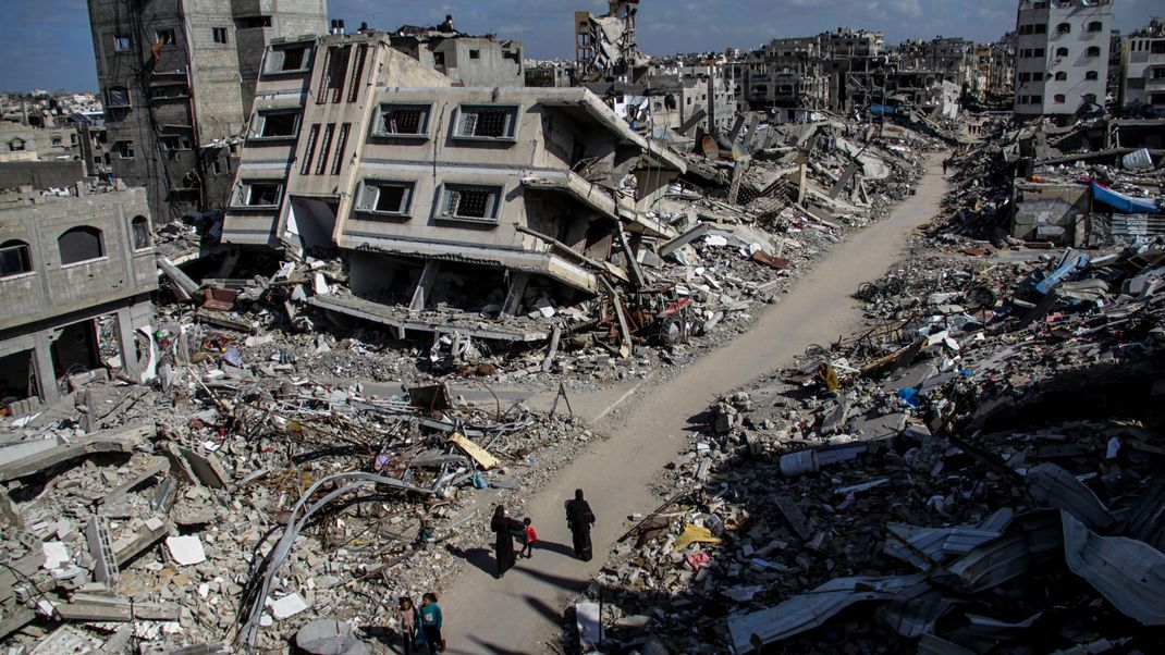 22.3.2024, Palästinensische Gebiete, Dschabalia: Menschen gehen an den Ruinen von Gebäuden vorbei, die durch israelischen Luftangriff im Flüchtlingslager Dschabalia zerstört wurden.