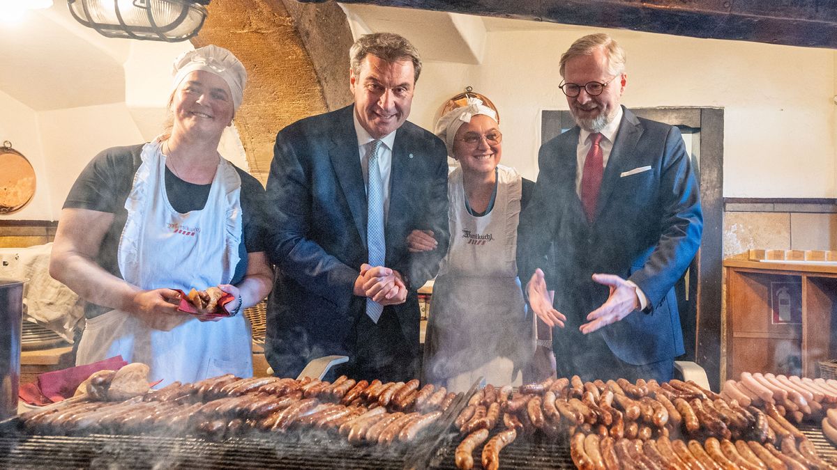 Petr Fiala, (r) Ministerpräsident der Tschechischen Republik und Markus Söder (CSU) stehen in der historischen Wurstkuchl, eine Bratwurststube, hinter einem Grill mit Bratwürsten.