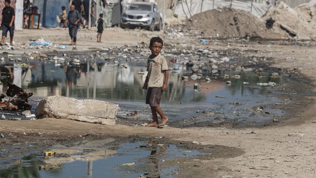 Ein Kind geht in der Nähe von Zelten, die als Unterschlupf in einer mit stehendem Abwasser bedeckten Straße dienen.&nbsp;