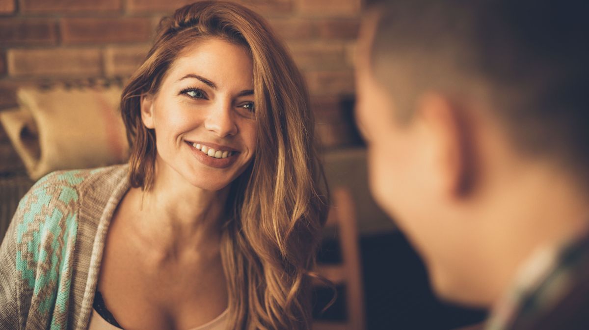 Young woman has a big smile while looking at a man at a table in a cafe