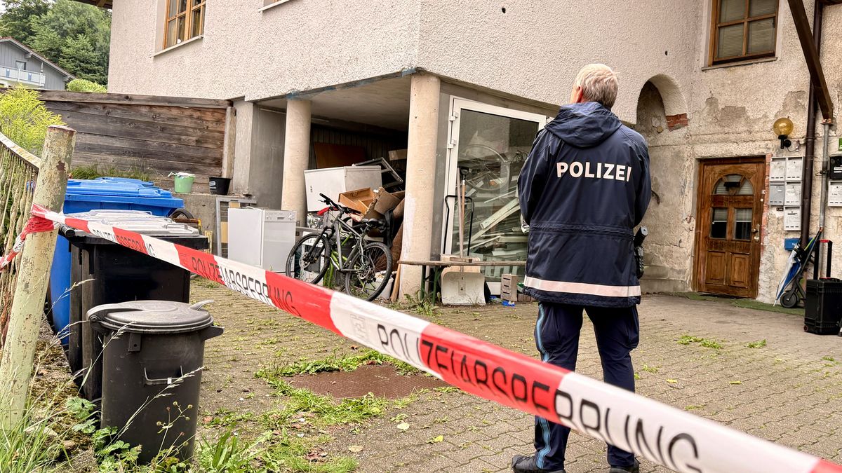 Ein Polizist steht hinter einer Absperrung vor einem Mehrfamilienhaus.