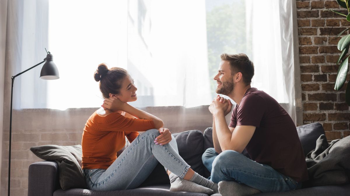 side view of young couple sitting on sofa and talking while looking at each other