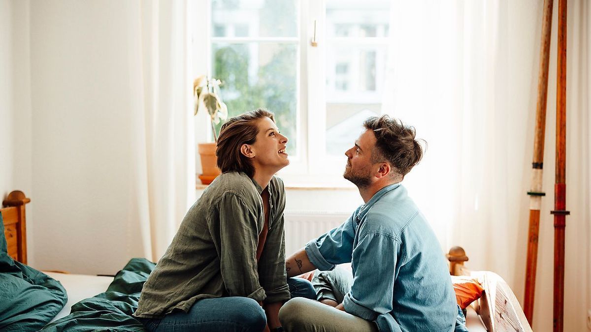 Smiling woman talking with man while sitting on bed at home