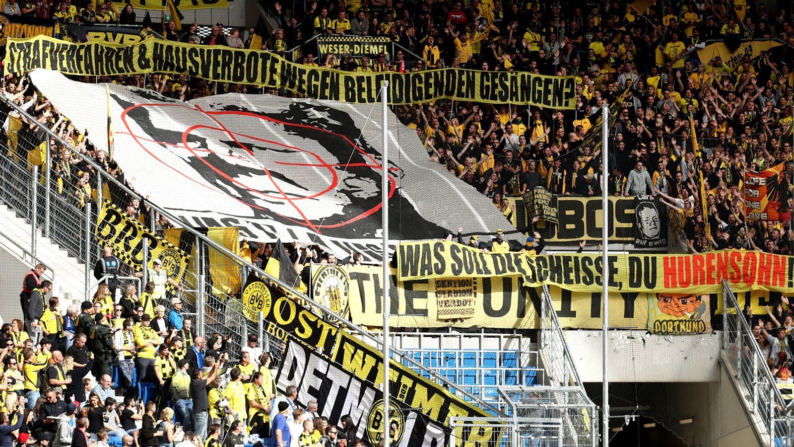 
                <strong>Der Grund für die Schmähungen</strong><br>
                Grund für die Ausschreitungen waren ausgerechnet die in München nicht gerade beliebten Ultras von Borussia Dortmund. Die aktive Fanszene des FC Bayern solidarisierte sich mit den Ultragruppierungen der Schwarz-Gelben im Streit gegen Kollektivstrafen. Hintergrund: Ein Fadenkreuz-Plakat in Richtung des SAP-Gründers führte dazu, dass das DFB-Sportgericht Anhänger von Borussia Dortmund für zwei Jahre von Auswärtsspielen in Sinsheim ausschloss. Und das, obwohl der DFB zu dieser Zeit Kollektivstrafen eigentlich ausgesetzt hatte. Hopp wurde für die aktive Fanszene zum Symbolbild für Kollektivstrafen. Proteste in zahlreichen deutschen Fankurven gegen den Milliardär waren die Folge.
              