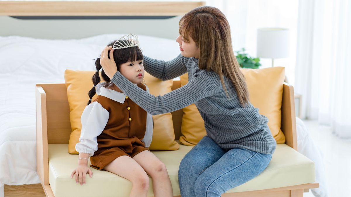Millennial Asian pretty young female teenager mother nanny babysitter role playing smiling wearing diamond princess crown on happy cheerful little cute preschooler daughter girl head