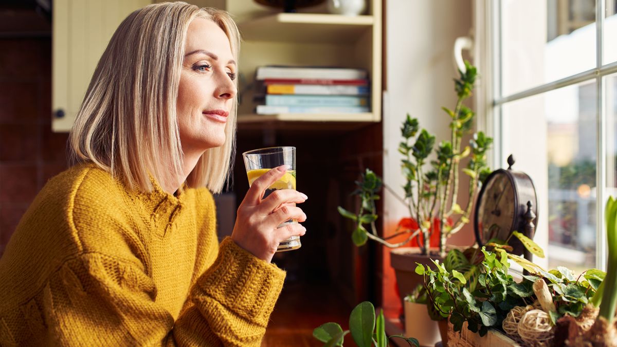 Frau trinkt ein Glas Wasser mit Zitrone am Fenster