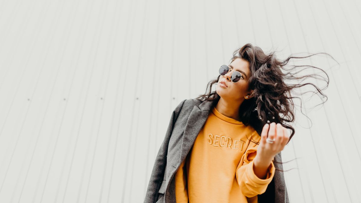 Portrait of stylish modern young curly woman in coat sunglasses. She smile at camera on the street and looks happy. Truly emotions.