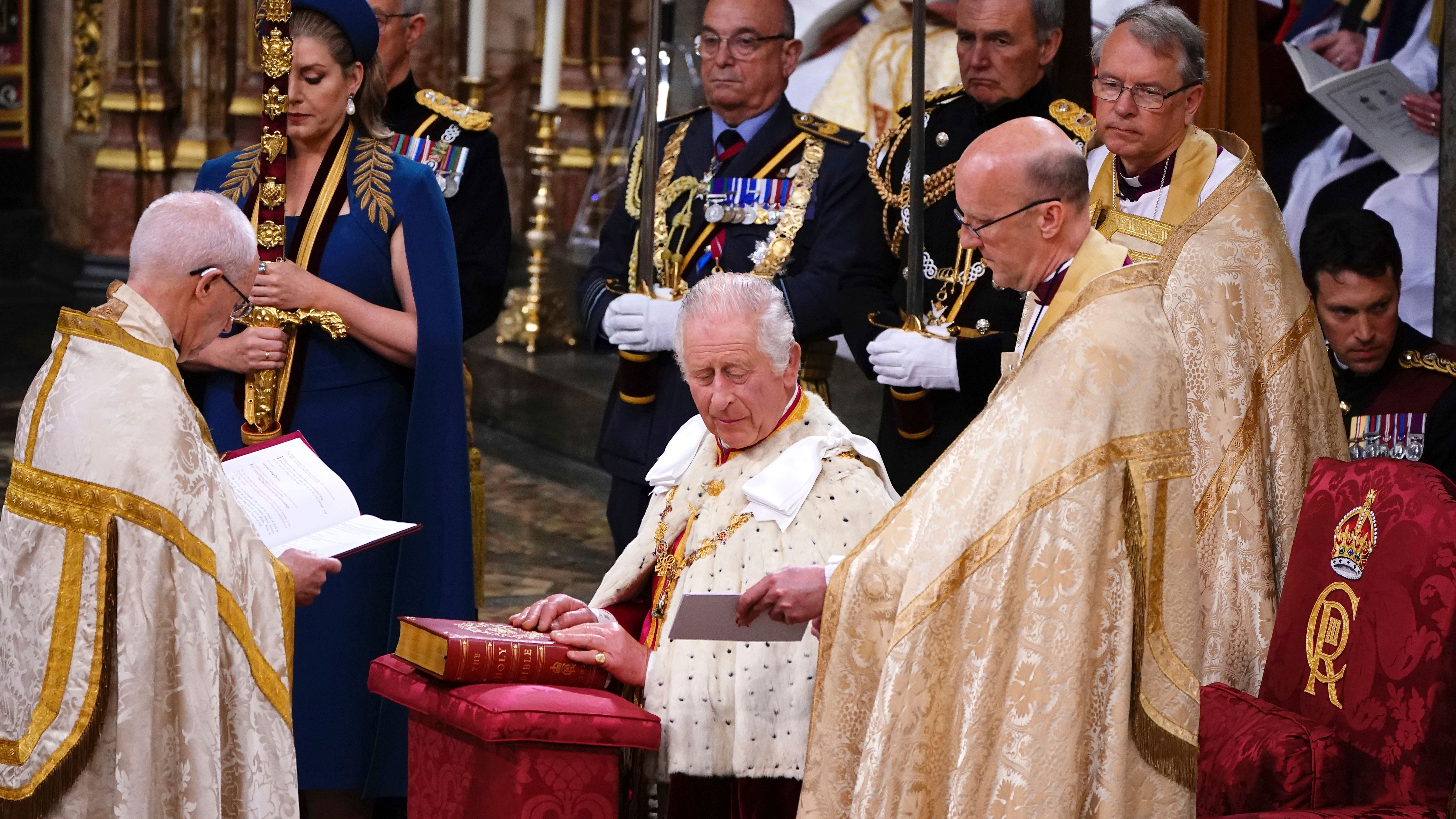 König Charles III. hält in Westminster Abbey seine Hände auf der Bibel.