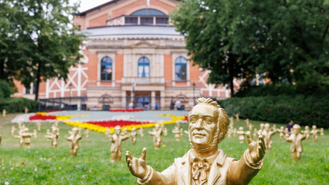 Goldfarbene Wagner-Figuren stehen vor dem Festspielhaus vor Beginn der Bayreuther Festspiele.
