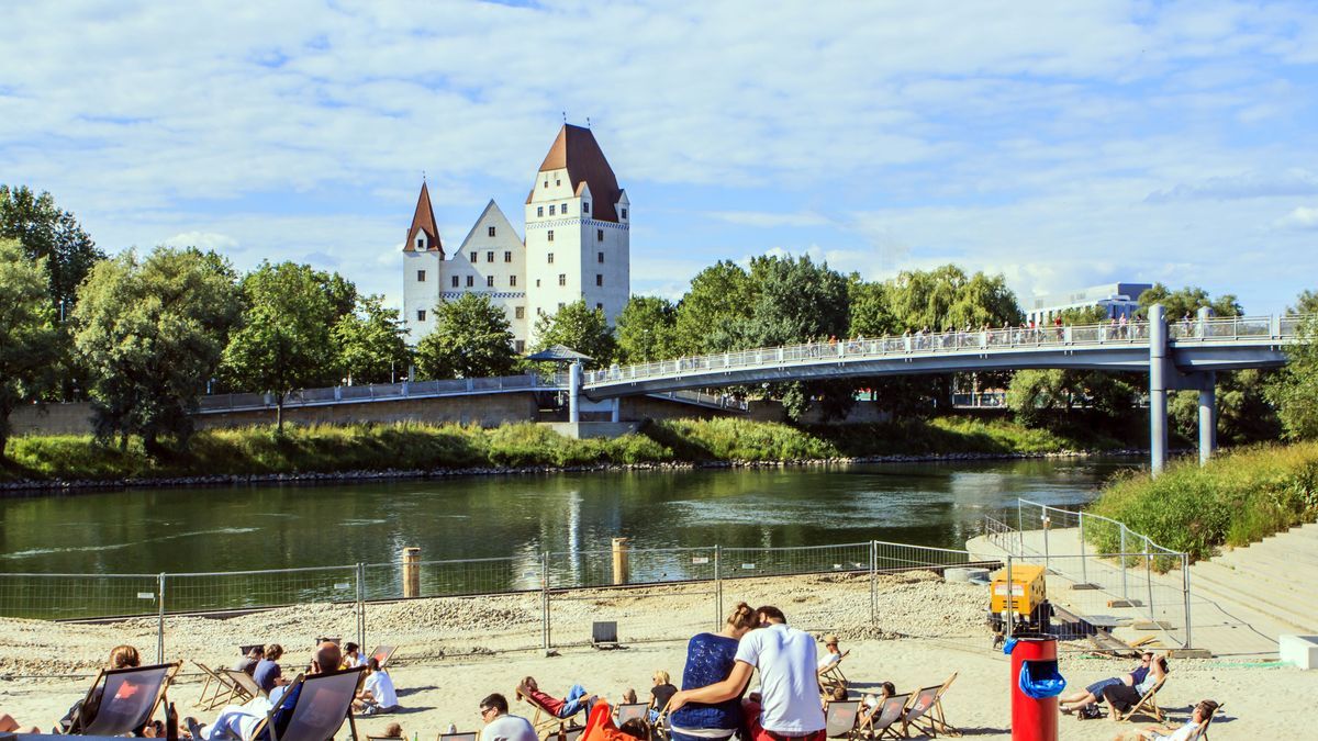 Menschen genießen die Sonne auf einem kleinen Strand auf den Banken an der Donau in Ingolstadt.
