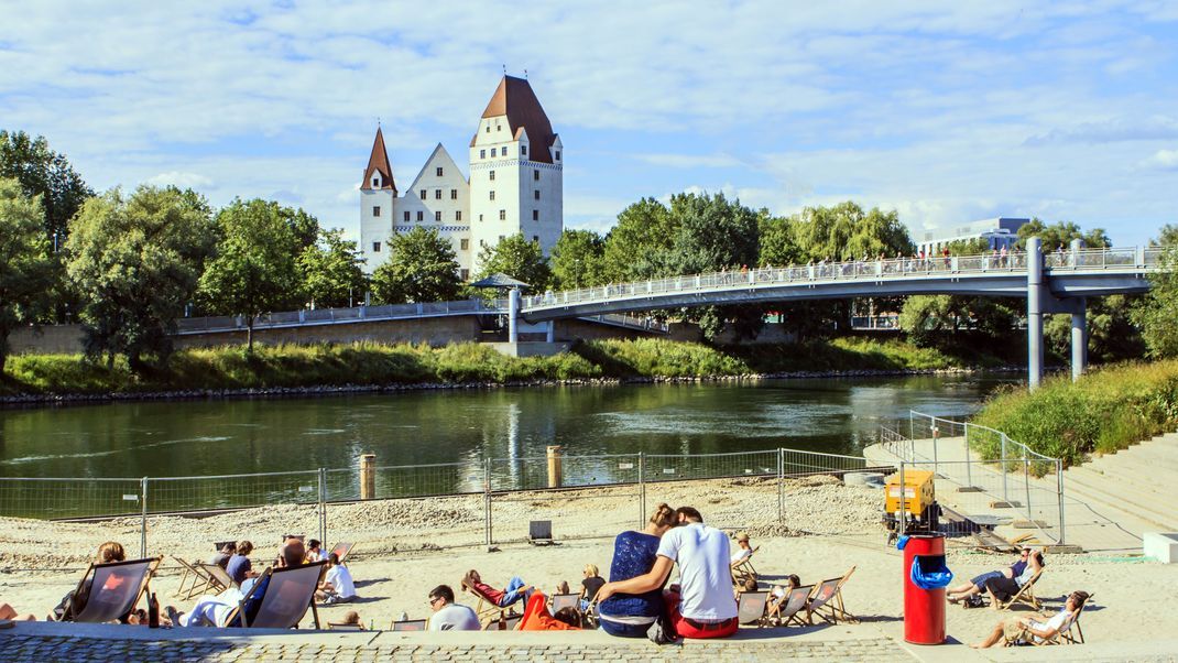 Menschen genießen die Sonne auf einem kleinen Strand auf den Banken an der Donau in Ingolstadt.