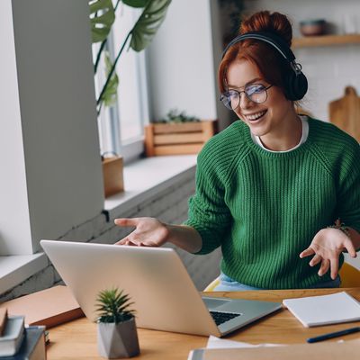 Cheerful young woman in headphones having web conference while working from home