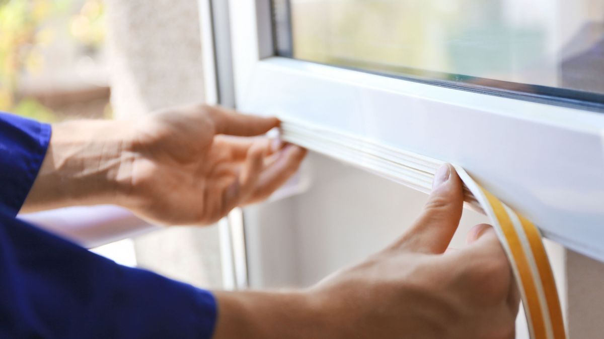 Construction worker putting sealing foam tape on window in house