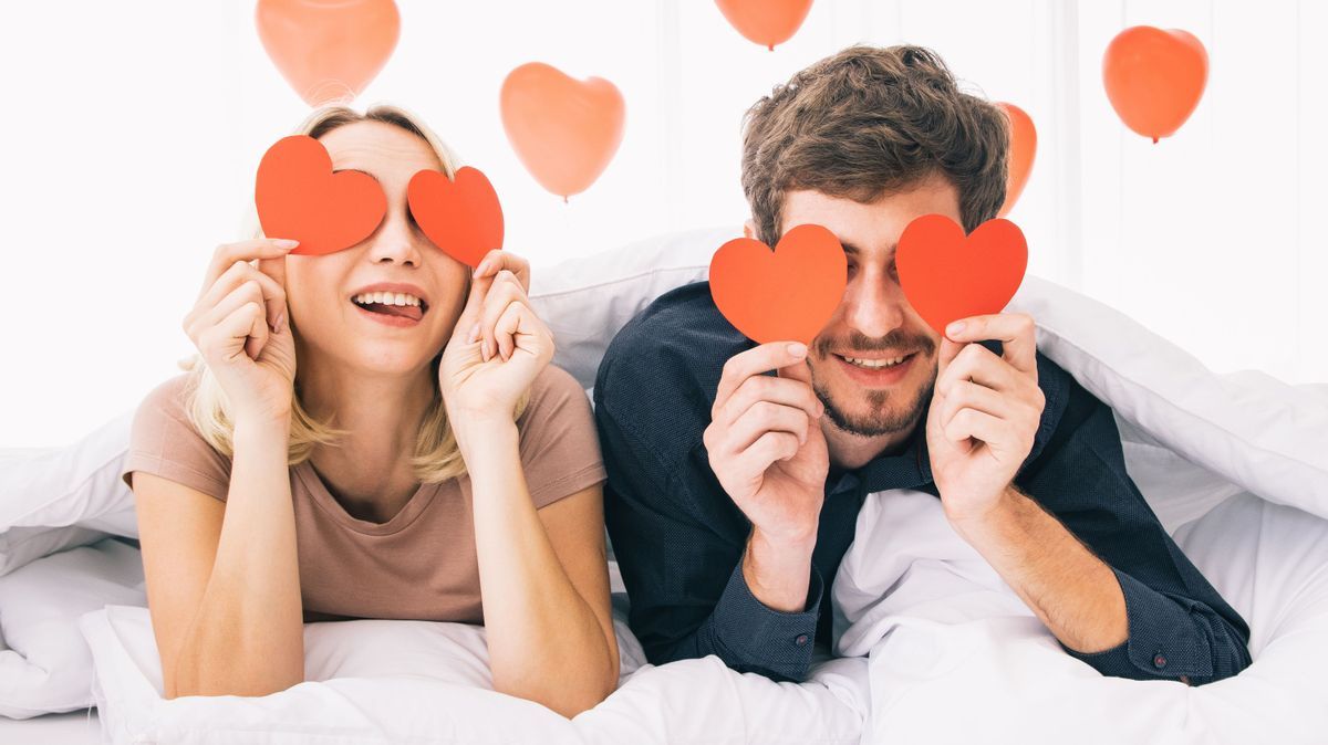 Close-up portrait of love couple attractive lovely girlish cheerful cheery girl holding in hands two heart symbol cards closing eyes on the bed. Holiday concept.