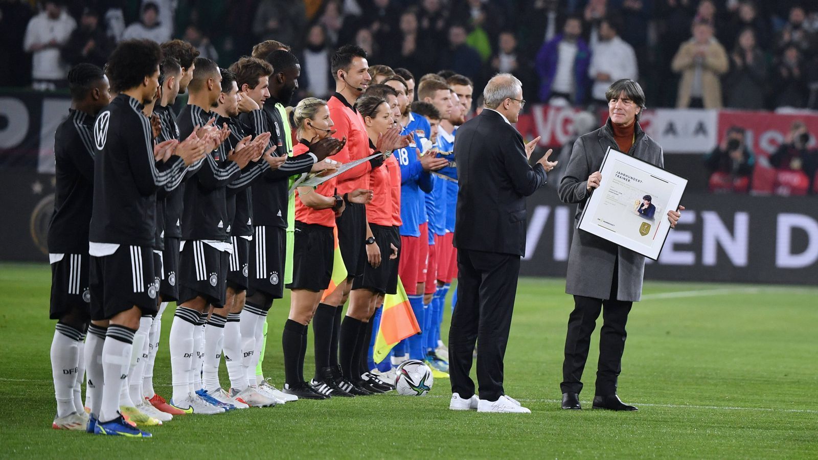 
                <strong>Vor Deutschland vs. Liechtenstein: Der Abschied von Ex-Bundestrainer Joachim Löw</strong><br>
                Dort übergibt DFB-Interimschef Peter Peters Löw höflich die Plakette als "Jahrhunderttrainer", mit der der einstige Bundestrainer zur aktuellen Mannschaft geht und Handshakes verteilt.
              