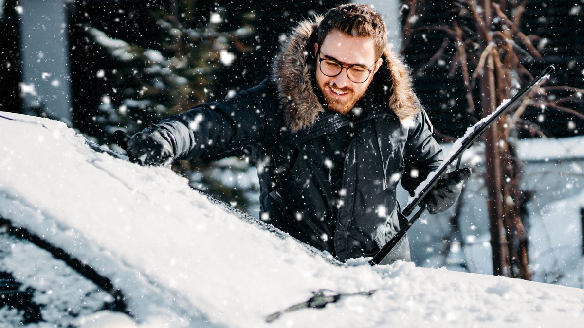 portrait of smiling man cleaning snow off his car during winter snowfall