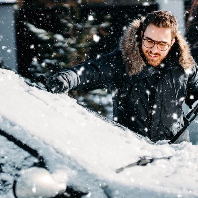 portrait of smiling man cleaning snow off his car during winter snowfall