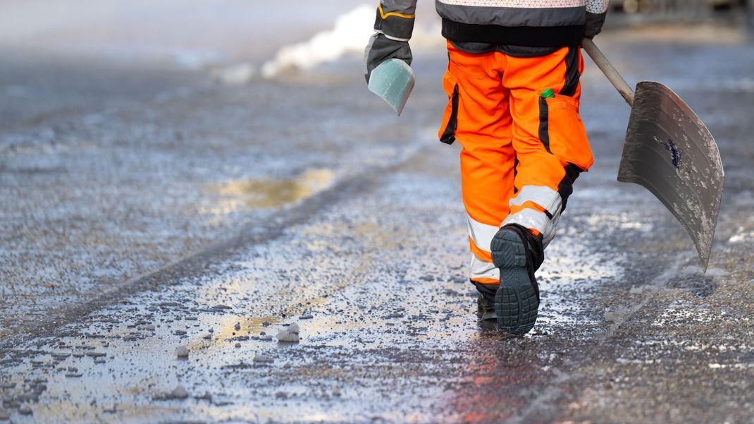 Ein Mitarbeiter vom Winterdienst der Stadt München geht mit einer Schneeschaufel über einen geräumten und gestreuten Fußweg. 