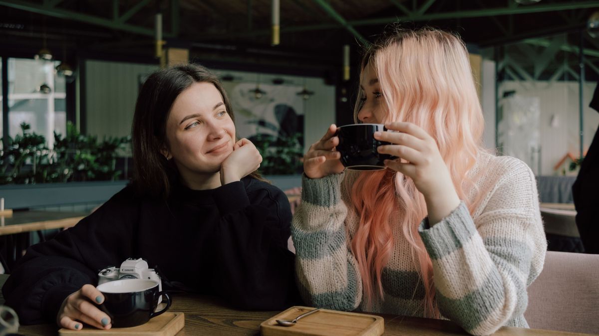 Interracial lesbian couple each other with shy smile, holding hands during lunch at restaurant.