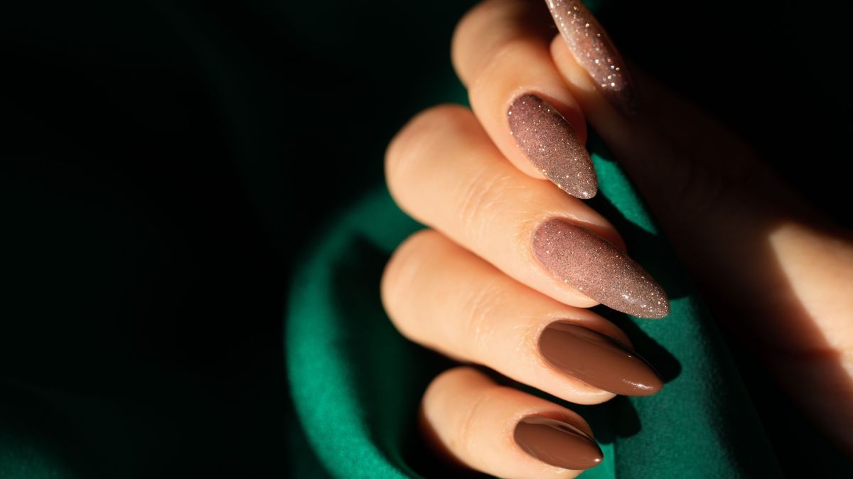 Female hand with a beautiful long nails in brown and shimmer color on a green silk background