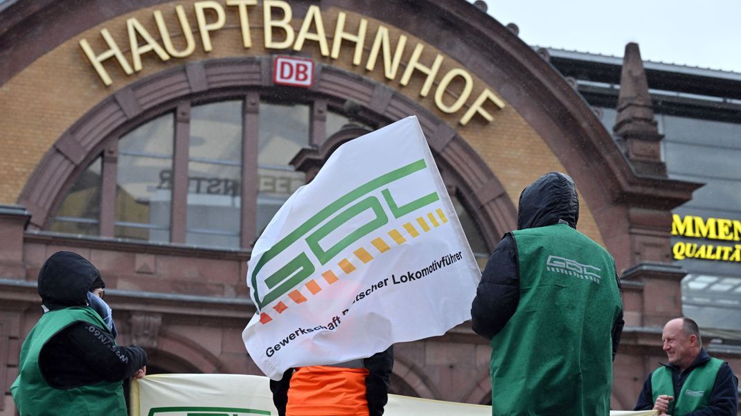 Gewerkschaftsmitglieder stehen mit Fahne und Transparent vor dem Erfurter Hauptbahnhof.