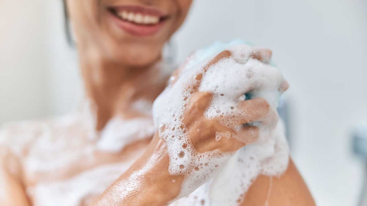 Cheerful young woman washing her body with bath loofah