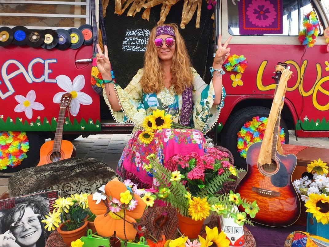 Eine Hippie-Frau zeigt vor einem Hippie-Bus im Jahr 2019 in Deutschland das Finger-V als Peace-Zeichen.