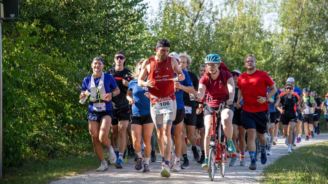 22. August 2024, Bayern: Extremsportler Jonas Deichmann (Mitte) wird bei seinem Langdistanz-Weltrekord von zahlreichen Läufer:innen an der Lände in Roth begleitet.